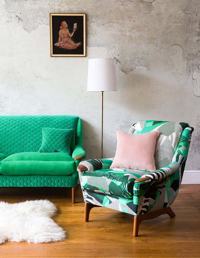 Reupholstered green sofa and patterned armchair against concrete background