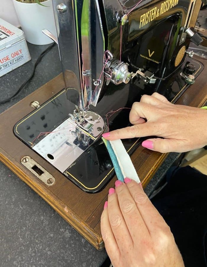 Sewing machine in use with two hands on fabric for double piping
