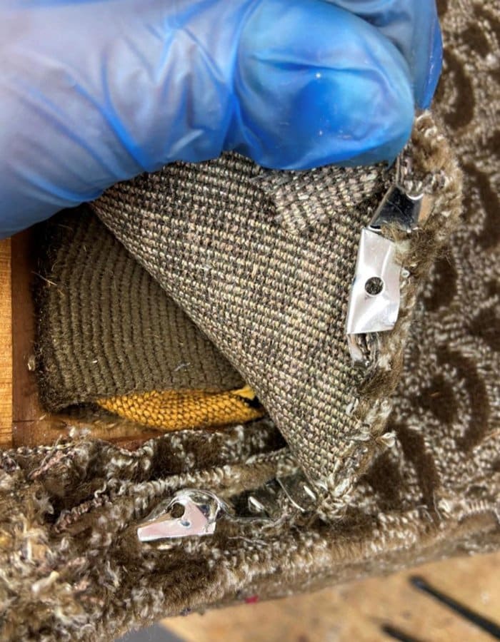 Silver-metal-ply-stuck-within-brown-material-held-up-by-blue-gloves-700x900