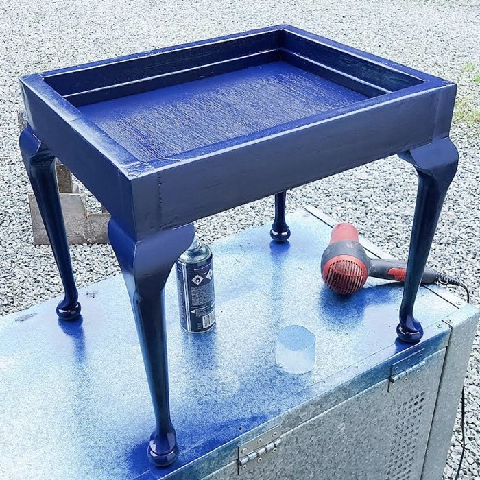 An old piano stool after being spray painted in dark blue paint for an upholstery project