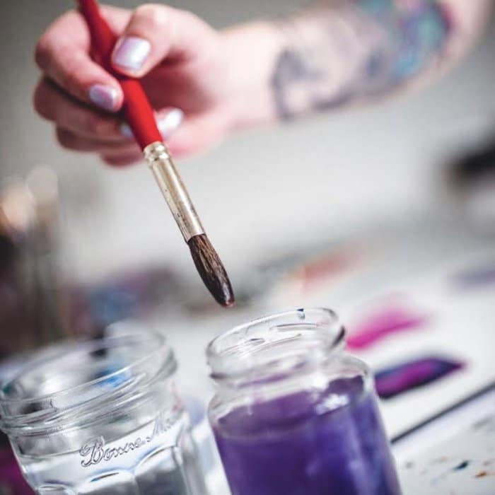 paint brush being dipped into purple paint to create a new upholstered surface design