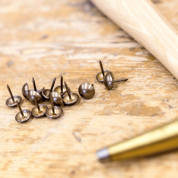 Brass upholstery nail pins lie next to a tack hammer on a workbench