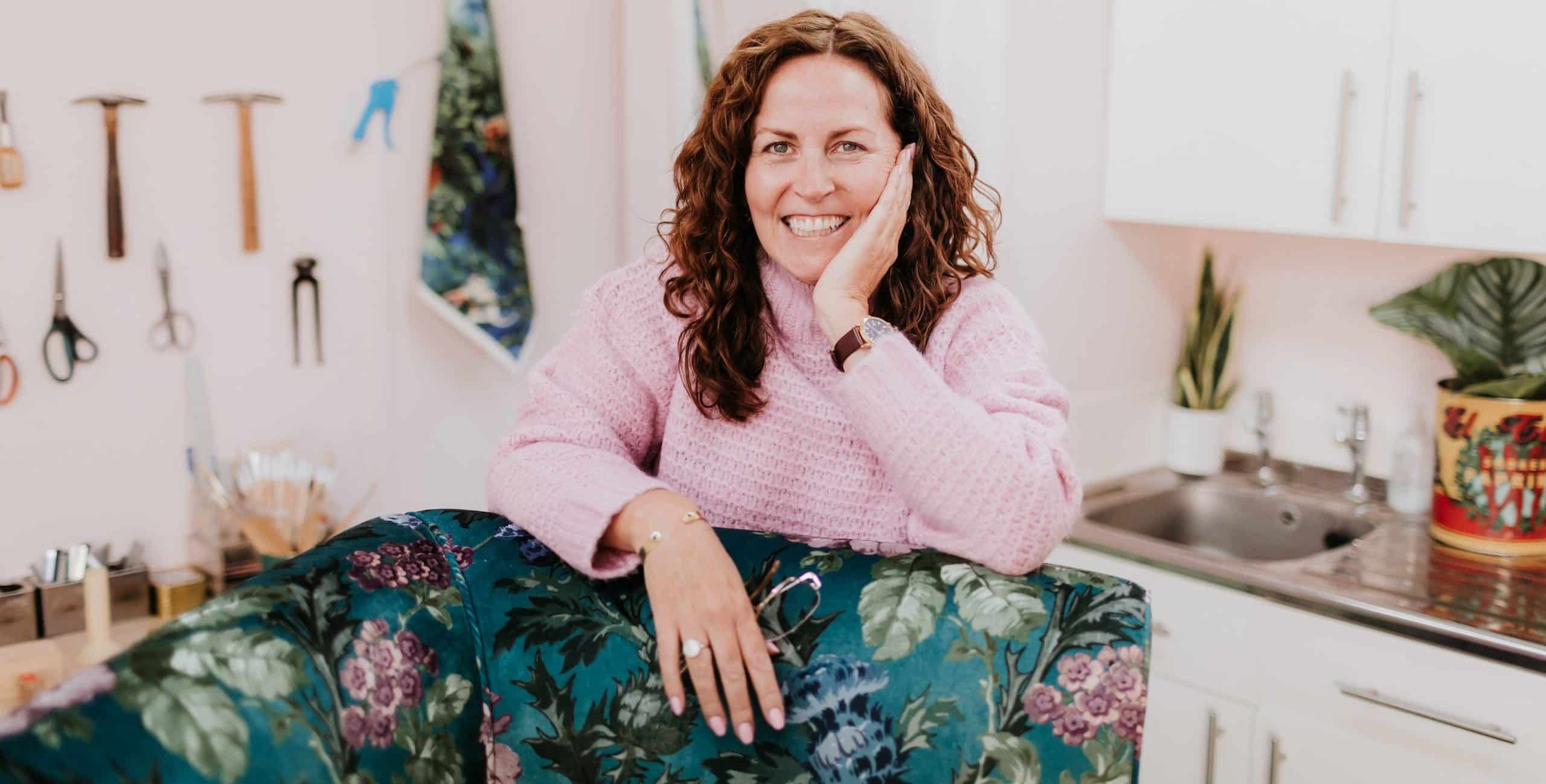 Sharon smiling whilst leaning on a green fabric covered chair