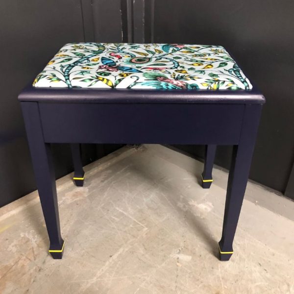 Piano stool with legs painted in navy blue with lime lines above the feet with a patterned fabric top