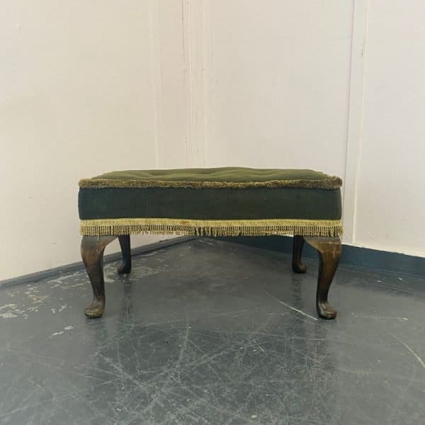 Footstool with dark legs, dark green fabric and pale fringing awaiting reupholstery