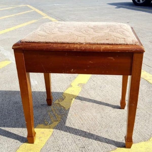 Piano stool with wooden legs and a pale fabric top awaiting reupholstery