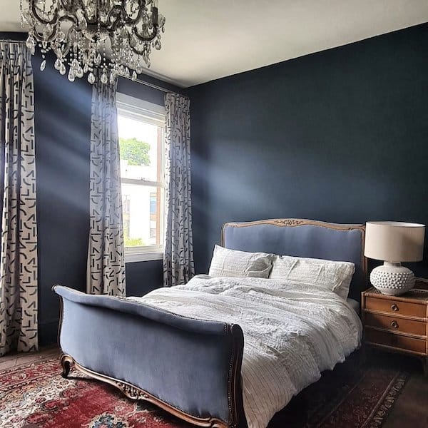 Reupholstered antique bedframe, in blue velvet in a bedroom with chandelier and dark patterned rug