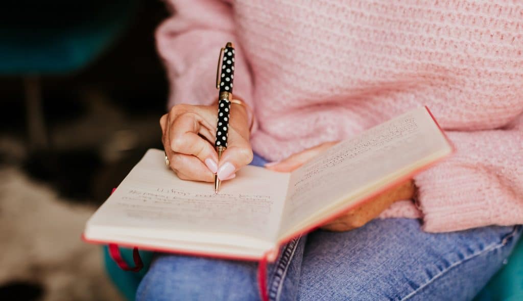 women writing in a notebook with a spotty pen