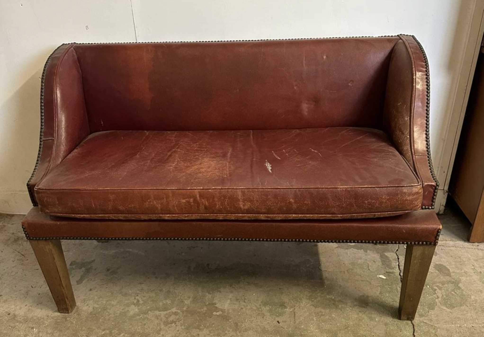 A two seater red leather bench seat with brass studded detail that was sold at Windsor Auctions