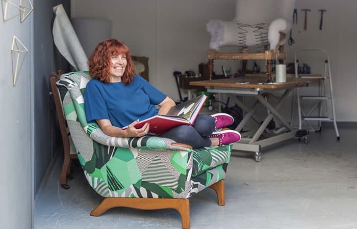 Sharon sat on a chair reupholstered in green pattern fabric in her workshop