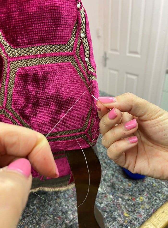 Deep pink fabric being sewn onto chair during upholstery process