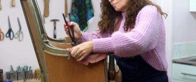 Sharon O'Connor working on a chair using her upholstery skill with upholstery tools on the wall in the background