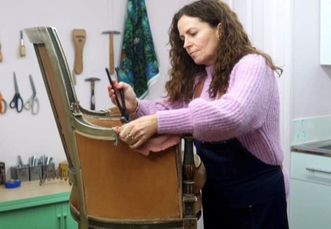 Sharon O'Connor working on a chair using her upholstery skill with upholstery tools on the wall in the background