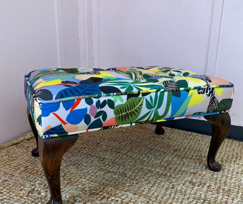 Upholstered footstool with wooden legs and covered in a funky print